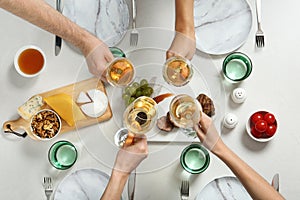 People holding glasses of white wine over table with tasty snacks