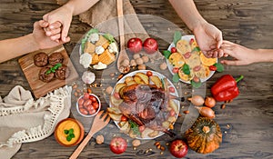 people holding hands, thanksgiving dinner served on wooden background, cooked turkey or chicken with vegetables