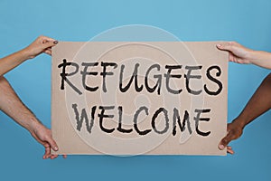 People holding sign with phrase WELCOME REFUGEES on light blue background, closeup