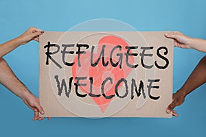 People holding sign with phrase WELCOME REFUGEES on light blue background, closeup