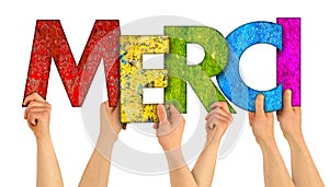 People holding up colorful rainbow wooden letter with the french word Merci english traslation: thank you isolated white