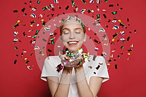 People, holidays, emotion and glamour concept. Happy young woman confetti against red studio wall banner background