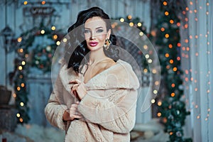 People, holidays and glamour concept - beautiful woman with makeup in fur coat and gold earrings over blue lights background.