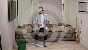 People, housework and housekeeping concept - happy man in headphones with mop cleaning floor and dancing at home. Using