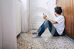 People inside home for stayhome lockdown emergency coronavirus - young man sit down on the. floor with a phone looking at the door photo