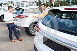 People inspect a car in the yard of a car dealership