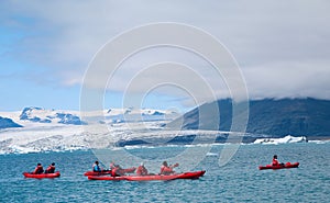 People kayaking in Jokulsarlon, glacial lagoon with icebergs surrounded by mountain range, Iceland
