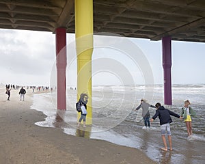 People lean into the wind under scheveningen pier on north sea beach in holland