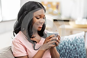 Happy african woman drinking tea or coffee at home