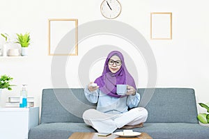 People and leisure concept,Young beautiful asian muslim woman in traditional dress wearing glasses sitting and watching TV,eating