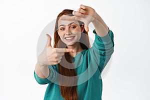 People and lifestyle. Happy redhead woman look through hand frames and smiling, imaging and getting creative, standing