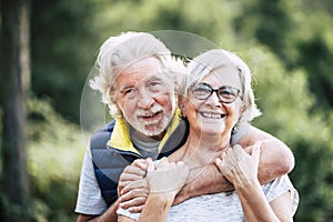 People in love at old age - couple of caucasian cheerful happy senior smile and hug in relationship - green defocused forest in