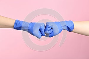 People in medical gloves doing fist bump on pink background, closeup of hands