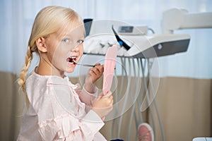 People, medical, stomatology and health care concept - Little girl examining her teeth with the help of dental mirrors
