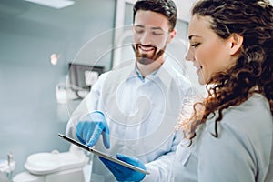 People, medicine, stomatology and health care concept - happy male dentist showing tablet pc computer to woman patient at dental