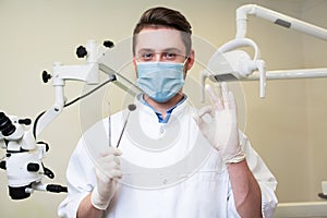 People, medicine, stomatology and healthcare concept - happy young male dentist with tools over medical office background