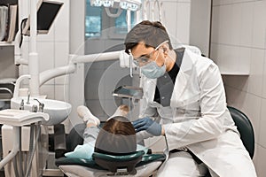 People, medicine, stomatology, technology and health care concept. Male dentist working with girl in clinic.