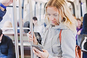 People in metro, commuters, woman passenger looking at the screen of her smartphone