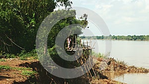 People and motorbikes driving over round bamboo bridge along the riverside 