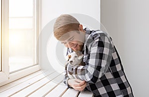 People, pet and dog concept - Young man over window background holding puppy Jack Russell Terrier