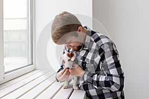 People, pet and dog concept - Young man over window background holding puppy Jack Russell Terrier