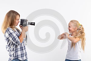 People, photography and hobby concept - woman using an old fashioned camera and photographing a little girl on white