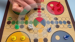 People play Ludo or Pachisi board game on beautiful wooden play board. Ludo is a strategy board game for two to four
