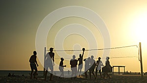 People play volleyball on the beach at sunset.