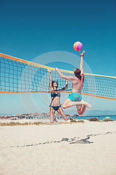 People playing beach volleyball having fun in sporty active lifestyle. Man hitting volley ball in game in summer. Woman