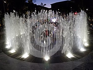 People playing in water fountain jets with lights at night