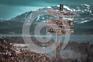 People with power are dangerous text quote engraved on wooden signpost outdoors in landscape looking polluted