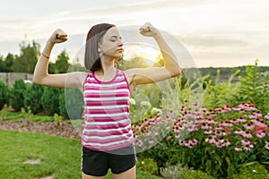 People, power, stamina, strength, health, sport, fitness concept. Outdoor portrait smiling teenage girl flexing her muscles, backg