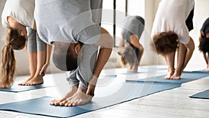 People practicing yoga at group lesson, standing in uttanasana pose