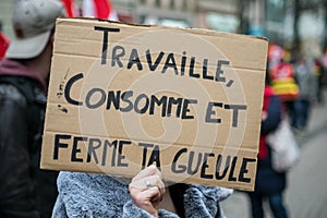 people protesting in the street with baner with tex in french : Travaille consomme et ferme ta gueule, traduction in