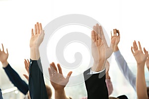 People raising hands to ask questions at business training on light background, closeup