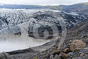 People in red and blue outdoor jackets dwarfed by a glacier on a cold, cloudy day in southern Iceland. Glacier falling