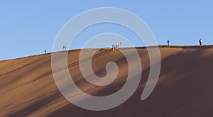 People on a red dune in the Namib Desert, in Sossusvlei, Namibia