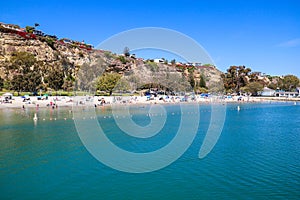 People relaxing on the beach and playing in the deep blue ocean water near a cliff covered with beach front homes on top