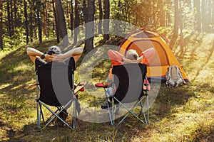 People relaxing in camping chairs at forest campsite and enjoying the nature