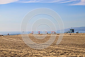 People relaxing in the vast brown silky sand at the beach with red umbrellas near a lifeguard station