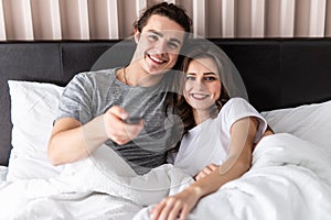 People, rest, love, relationships and television concept. Happy couple with remote lying in bed at home and watching tv