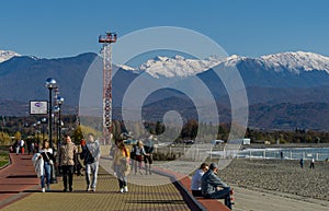 People resting on sunny winter day on Olympic Embankment in Sirius against Caucasus mountains