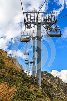 People ride on chair ski lift of Gorky Gorod mountain resort on autumn Caucasus mountains background. Sochi, Russia