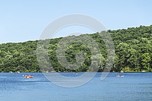 People riding in kayaks and canoe on Sheppard lake, forest in the background and blue sky, New Jersey Botanical Garden