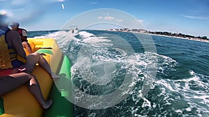 People riding on water inflatable attraction with motor boat Banana on sea