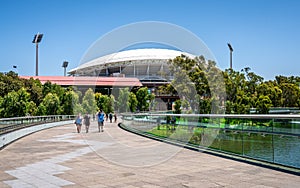 People on riverbank curved footbridge over torrens river and Adelaide Oval stadium in background in Adelaide SA Australia