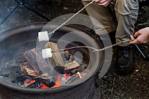 People roasting large marshmallows on a stick over the campfire firepit. Camping family fun