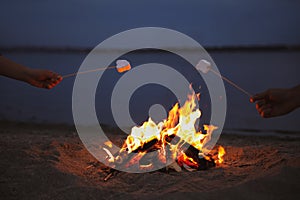 People roasting marshmallows over burning firewood on beach, closeup