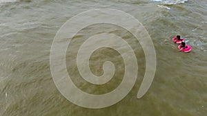People in rubber rings swim on the waves in the sea. Aerial video