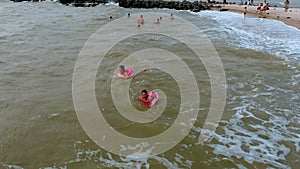 People in rubber rings swim on the waves in the sea. Aerial video